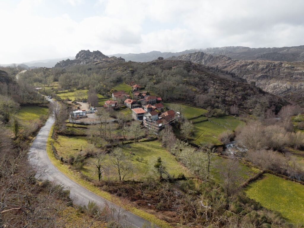 A aldeia no fundo do vale, com a estrada a curvar e a serra de granito atrás