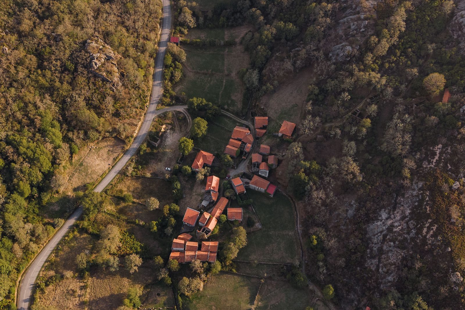 A aldeia de Varziela vista de cima ao fim da tarde, com os telhados de telha, a estrada e a mata à volta