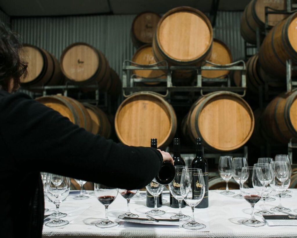 Vinho a ser servido numa adega, com barricas e copos na mesa