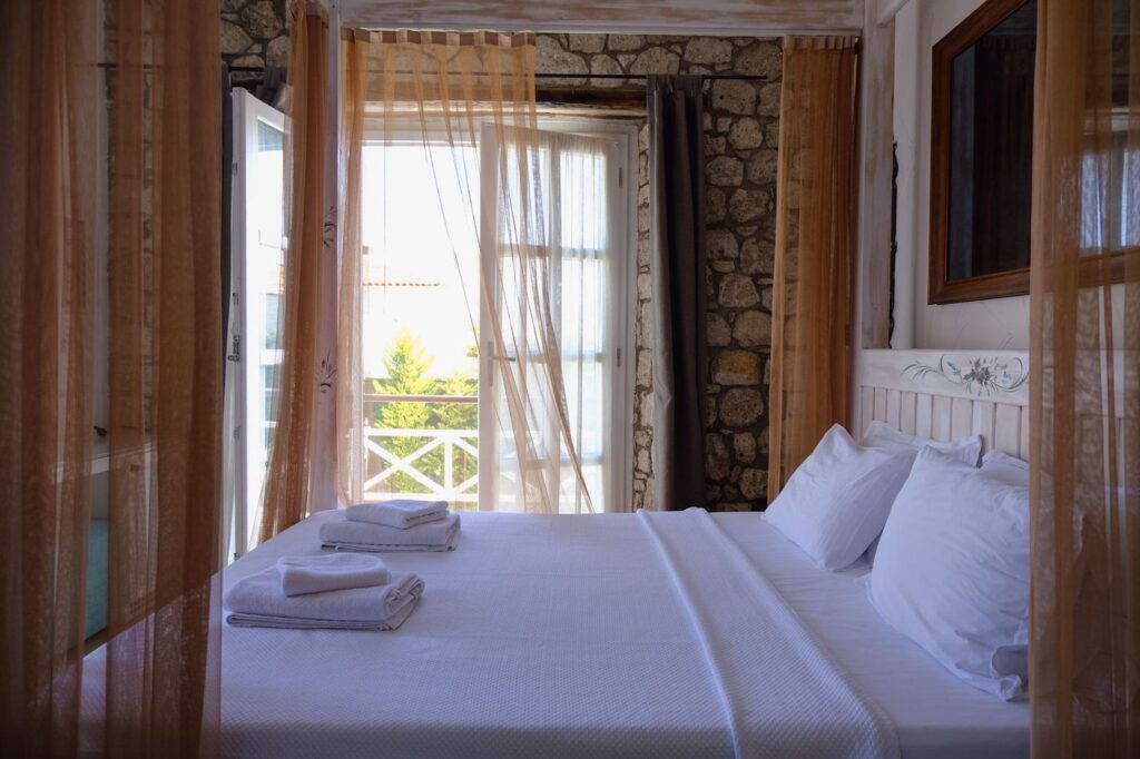 Quarto de hotel com paredes de pedra, cama de linho branco e janela para o jardim