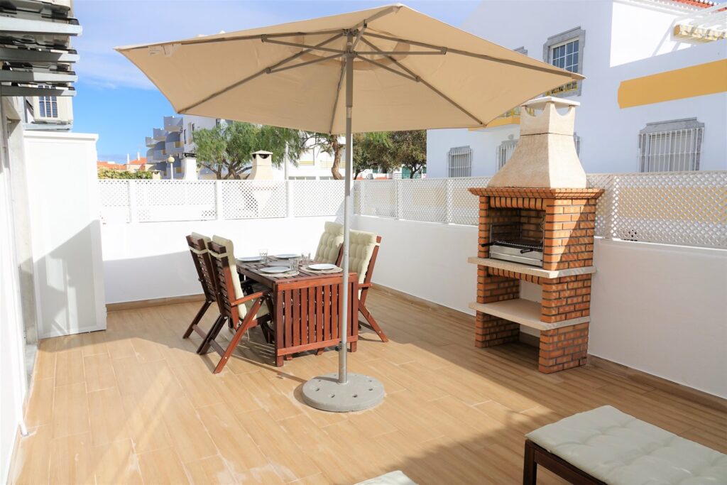 Terraço de um apartamento do Altura da Maré, com mesa posta, grelhador e espreguiçadeiras